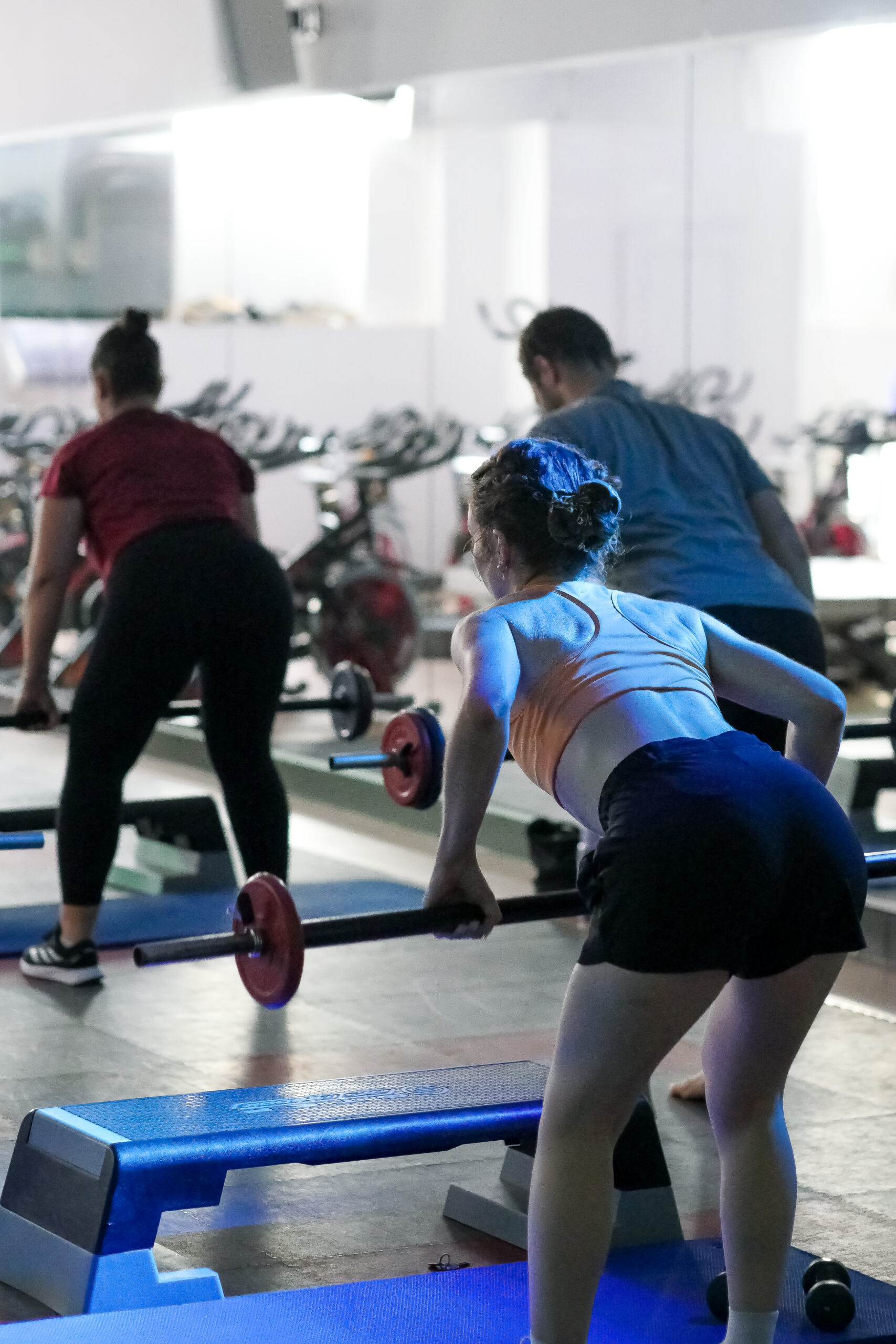 cours de pump and bike salle de sport avec piscine o-zone bordeaux trois adhérents effectuent un mouvement de tirage avec une barre et des disques de poids